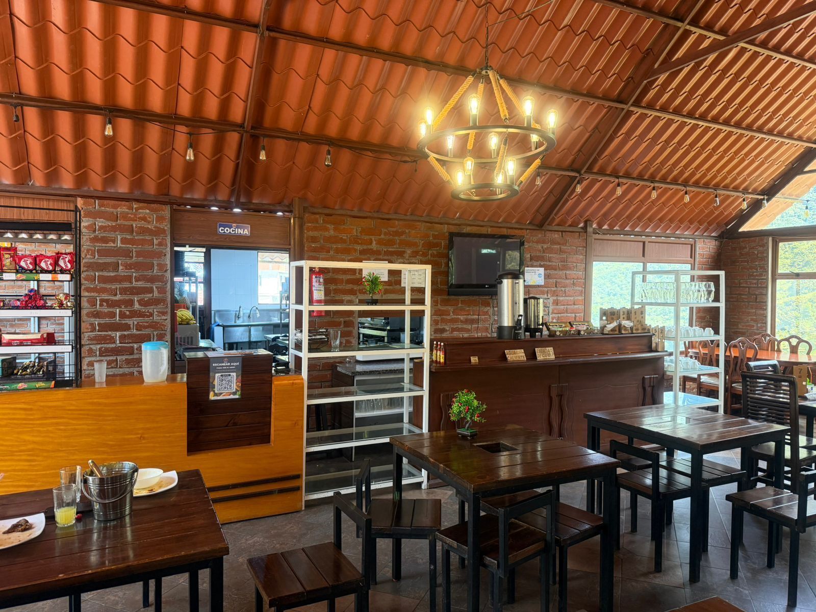 A restaurant interior with brick walls, wooden tables and chairs, a bar area, and a television screen.