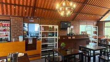 A restaurant interior with brick walls, wooden tables and chairs, a bar area, and a television screen.