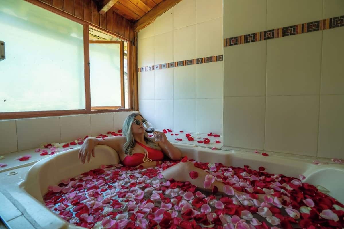 Una donna in una vasca da bagno piena di petali di rosa, con una finestra e pareti piastrellate sullo sfondo.