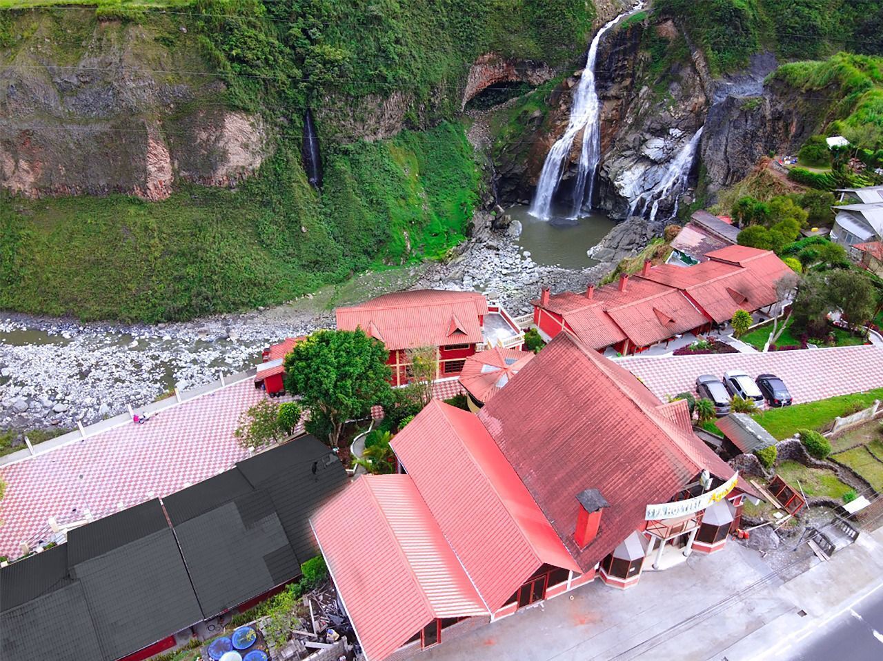 Um hotel com telhados vermelhos, um rio e uma cascata ao fundo.