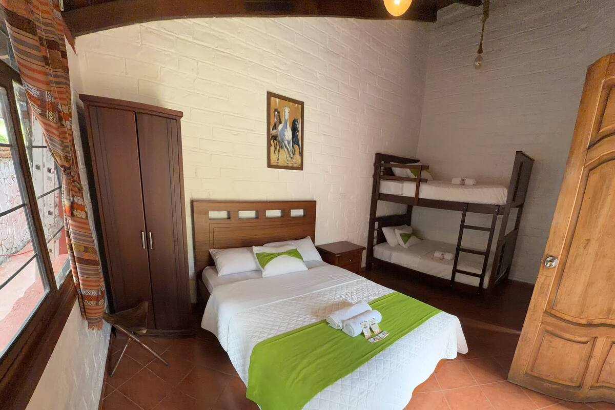 Una camera da letto con un letto, una cuccetta, un armadio in legno, un quadro appeso e una finestra con tende.