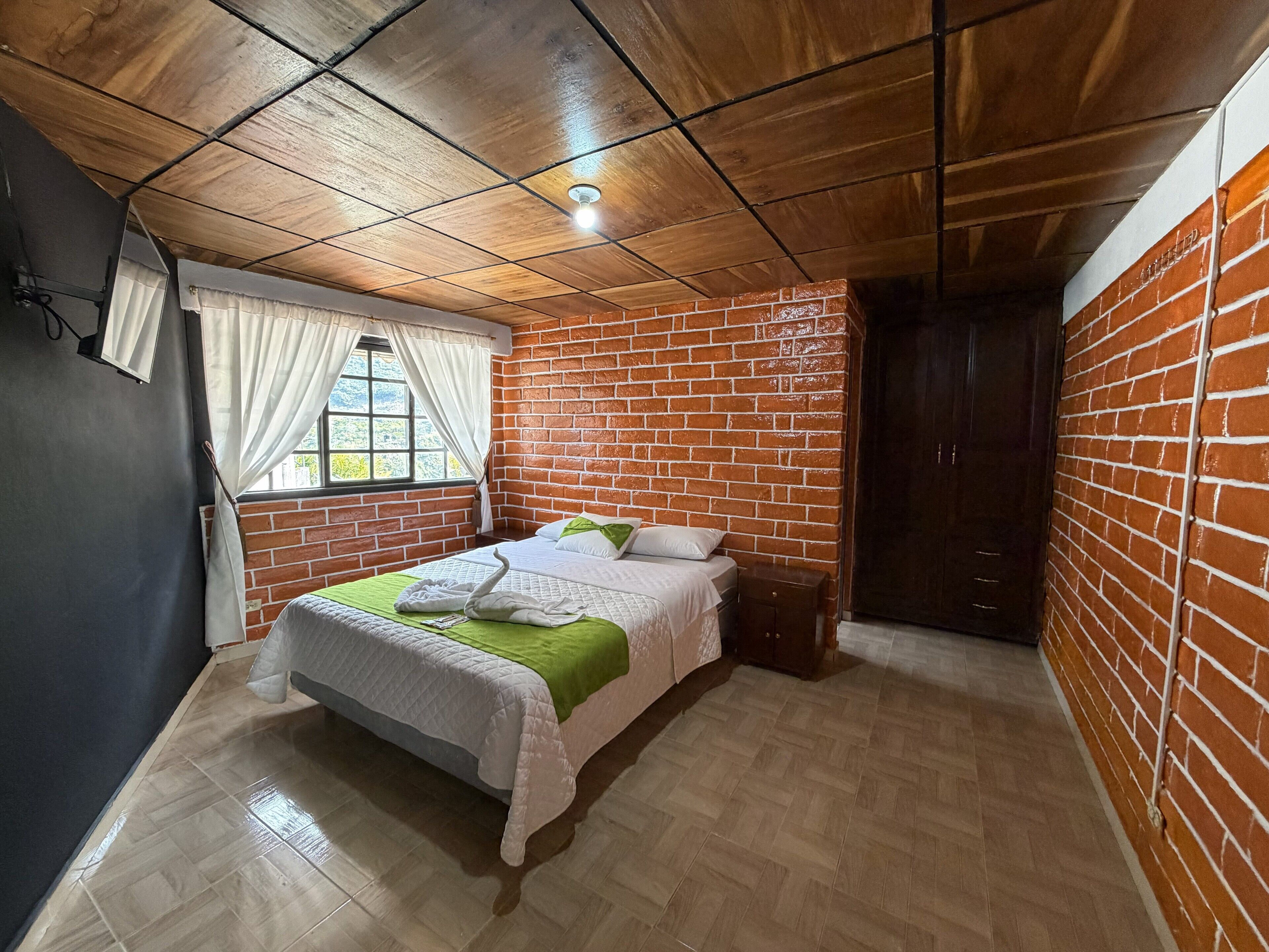 Un dormitorio con pared de ladrillo, techo de madera y cama con manta verde.