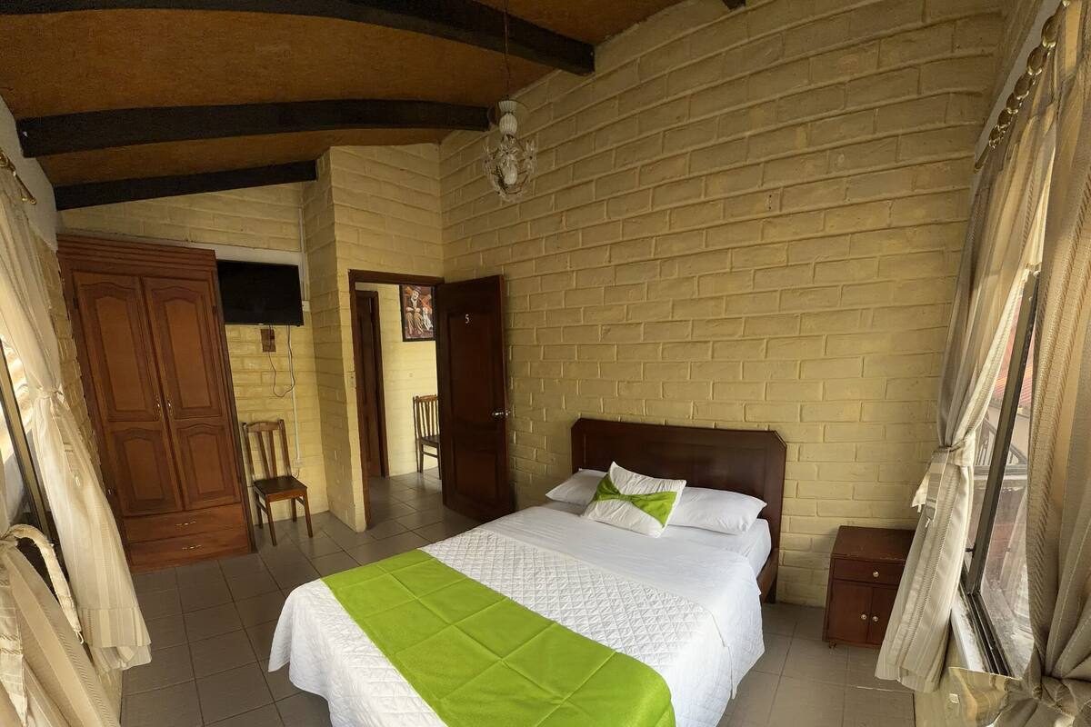 Una camera d'albergo con un letto, un armadio in legno, una sedia e una porta che dà su un'altra stanza.