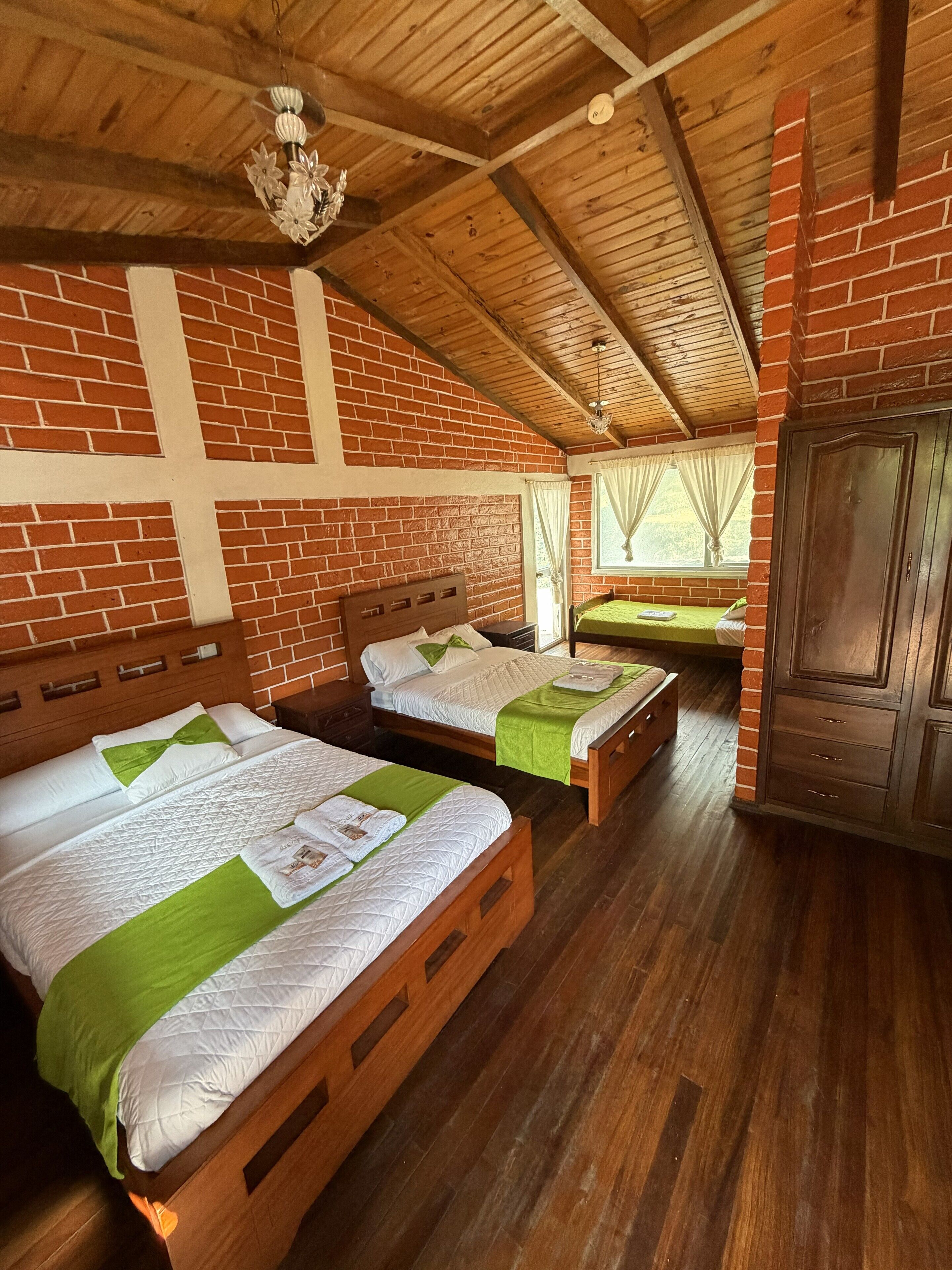 A room with two wooden beds, a brick wall, and a wooden ceiling.