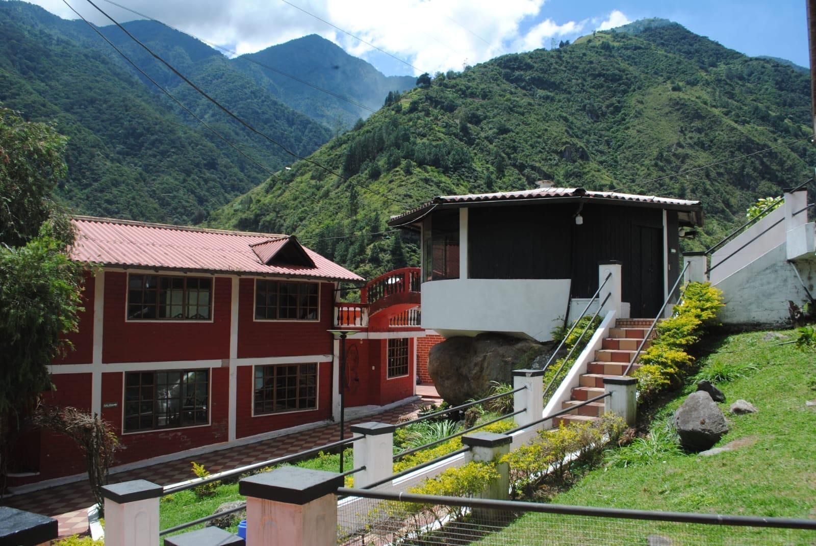 A red building with a balcony, a staircase leading to a black-roofed structure, and a mountainous backdrop.