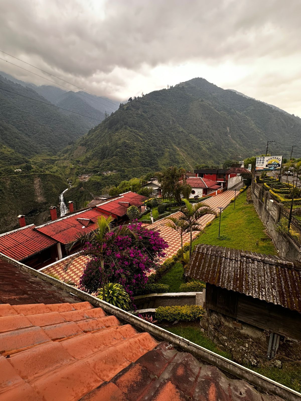 A mountainous landscape with a red-roofed building, a sign for 'Hosteria Agayan', and a lush green valley.