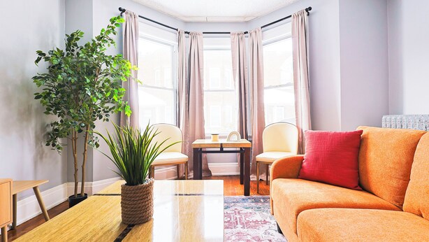 A corner room with a wooden table, two chairs, a sofa, a potted plant, and a view through large windows. - Cozy Modern 3BR by Downtown & Beach + Free Parking (Cleveland)