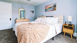 A bedroom with a bed, nightstand, dresser, and a painting on the wall. - Cozy Modern 3BR by Downtown & Beach + Free Parking (Cleveland)