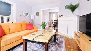 A living room with a sofa, coffee table, TV, fireplace, and a dining area with chairs and a table. - Cozy Modern 3BR by Downtown & Beach + Free Parking (Cleveland)