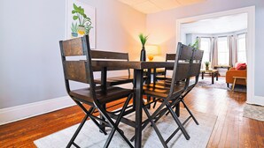 A dining area with a wooden table and chairs, a vase with a plant, and a painting on the wall. - Cozy Modern 3BR by Downtown & Beach + Free Parking (Cleveland)