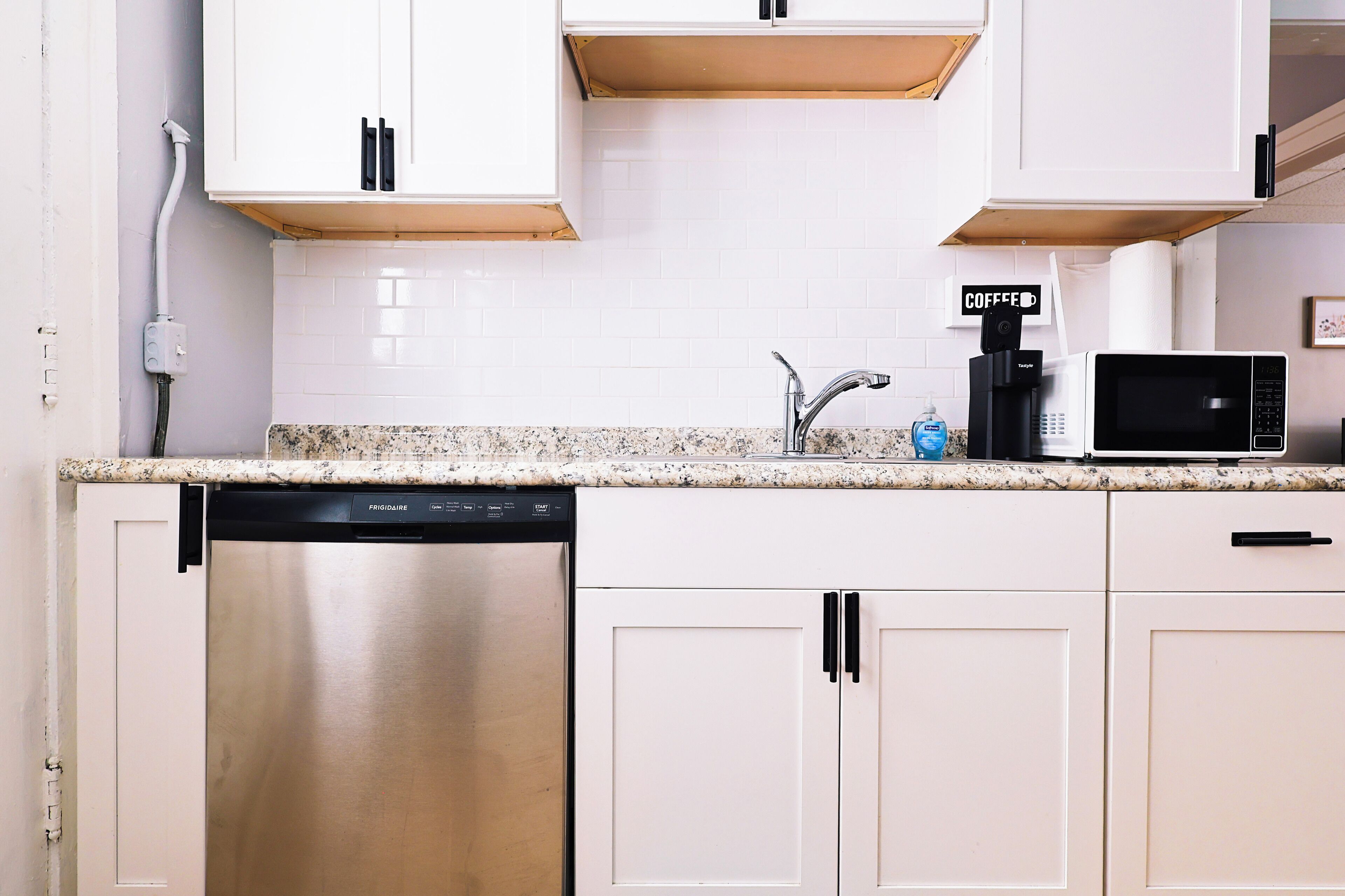 A kitchen with white cabinets, a stainless steel dishwasher, a coffee maker, and a microwave.