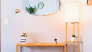 A wooden console table with a small potted plant, a WiFi sign, a round mirror, and a floor lamp. - Cozy Modern 3BR by Downtown & Beach + Free Parking (Cleveland)