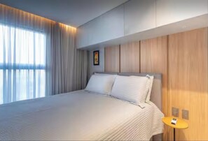 Ein modernes Hotelzimmer mit einem großen Bett, einem hölzernen Kopfteil und einem kleinen Tisch mit einer Lampe.