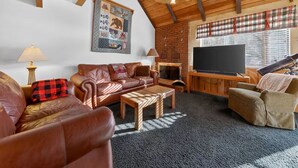 Una sala de estar acogedora con chimenea, sofás de cuero, un televisor de pantalla plana y un ventilador de techo.