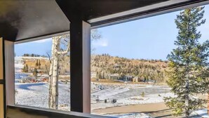 Vista desde una ventana con marco de madera, con un paisaje nevado que incluye árboles y edificios.