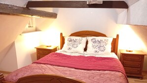 A wooden bed with a pink quilt, two bedside tables with lamps, and floral-patterned pillows. - Apartment 44 m2 Located in a quiet village.  Shops nearby. (Kesseldorf)