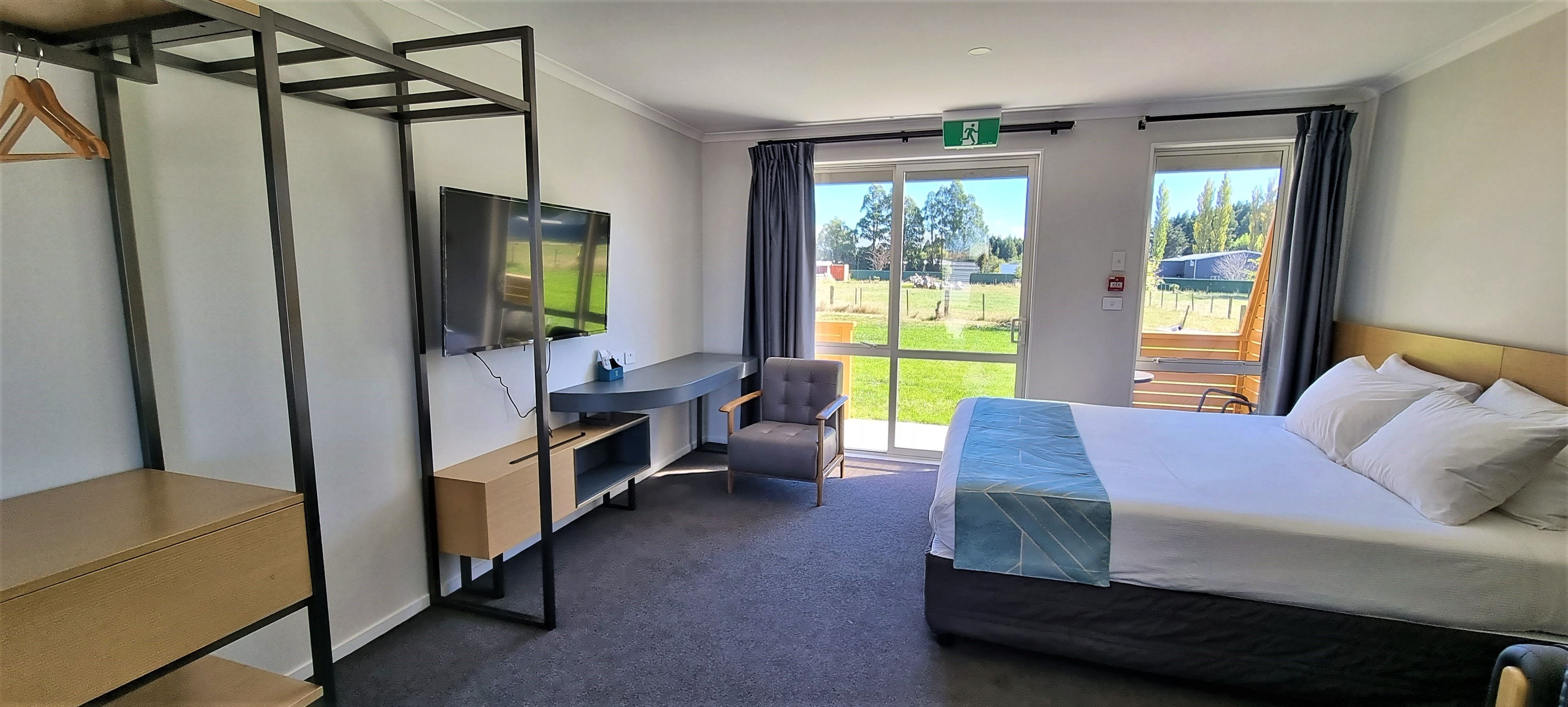 A hotel room with a bed, a desk, a chair, a TV, and a view of the outdoors.