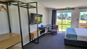 Et hotelværelse med seng, skrivebord, stol, fjernsyn og udsigt til det fri.