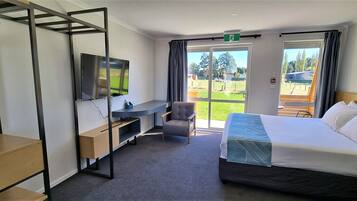 A hotel room with a bed, a desk, a chair, a TV, and a view of the outdoors.