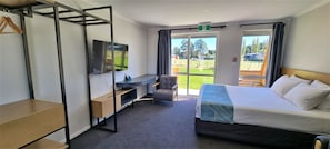 A hotel room with a bed, a desk, a chair, a TV, and a view of the outdoors.
