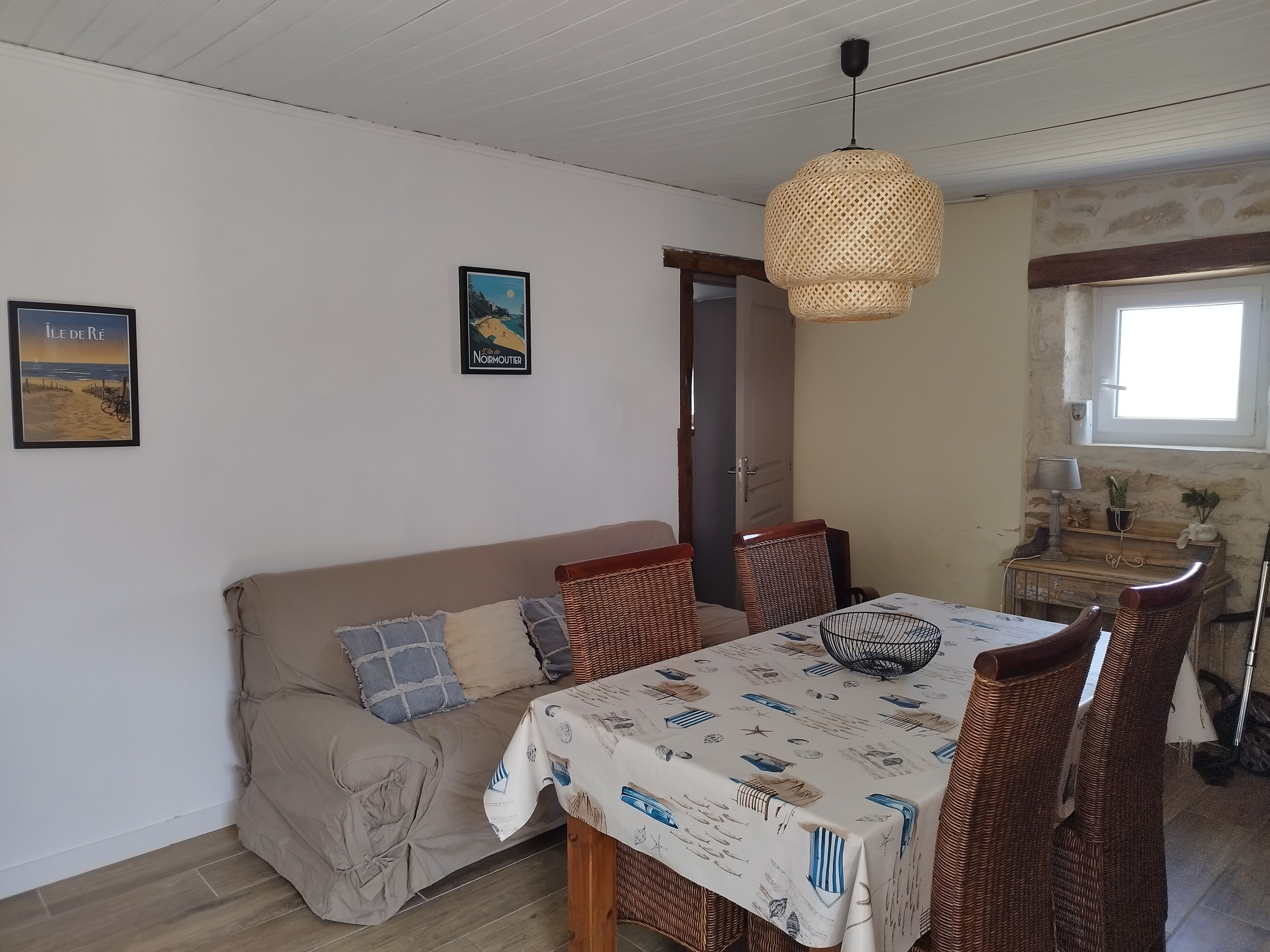 Ein gemütliches Zimmer mit einer Couch, einem Esstisch, Korbstühlen, einer Hängeleuchte und einem Bild an der Wand.