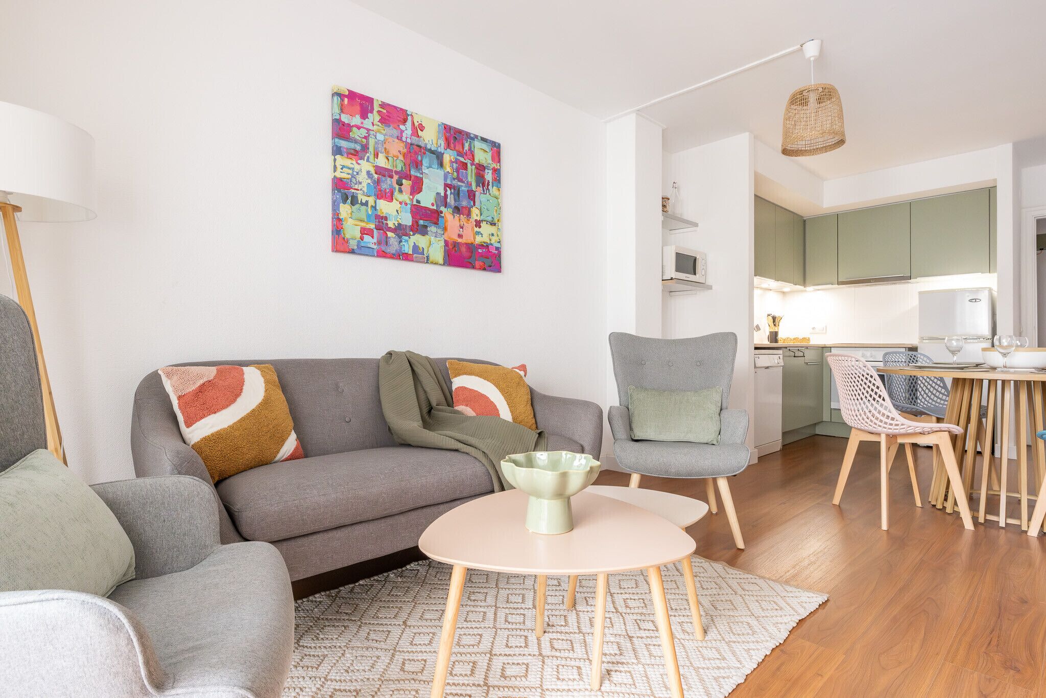 Een moderne woonkamer met een grijze bank, een ronde tafel en een kleurrijk abstract schilderij aan de muur.