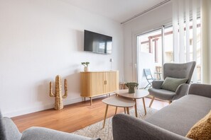 A modern living room with a flat-screen TV, a wooden cabinet, a cactus, a grey armchair, and a small table. - Apartment at 260 m from the beach, recently renovated (L'Escala)