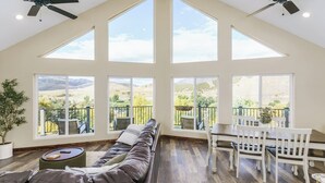 Ein geräumiges Wohnzimmer mit hoher Decke, großen Fenstern und einem Balkon mit Gartenmöbeln.