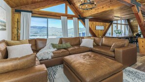 Ein geräumiges Wohnzimmer mit einer großen Eckcouch, Holzbalken und Blick auf die Berge.