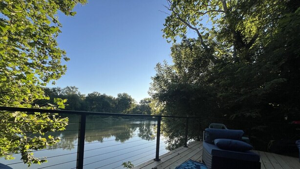 Una terraza de madera con barandilla que da a un lago tranquilo, rodeada de árboles.