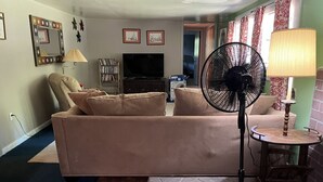 Una sala de estar con un sofá color beige, un ventilador negro, una mesita redonda y una lámpara.