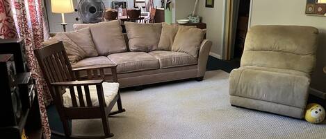 Una sala de estar con un sofá color beige, una silla de madera, un sillón color beige y un pequeño juguete amarillo en el suelo.