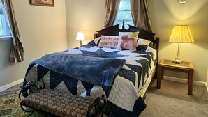 Un dormitorio con una cama, dos lámparas de noche, una ventana con cortinas, un reloj de pared y un cuadro enmarcado.