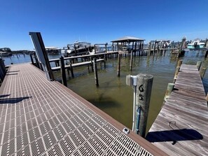 Eine Holzsteg erstreckt sich über ein Gewässer, an dessen Ufer Boote vertäut sind.