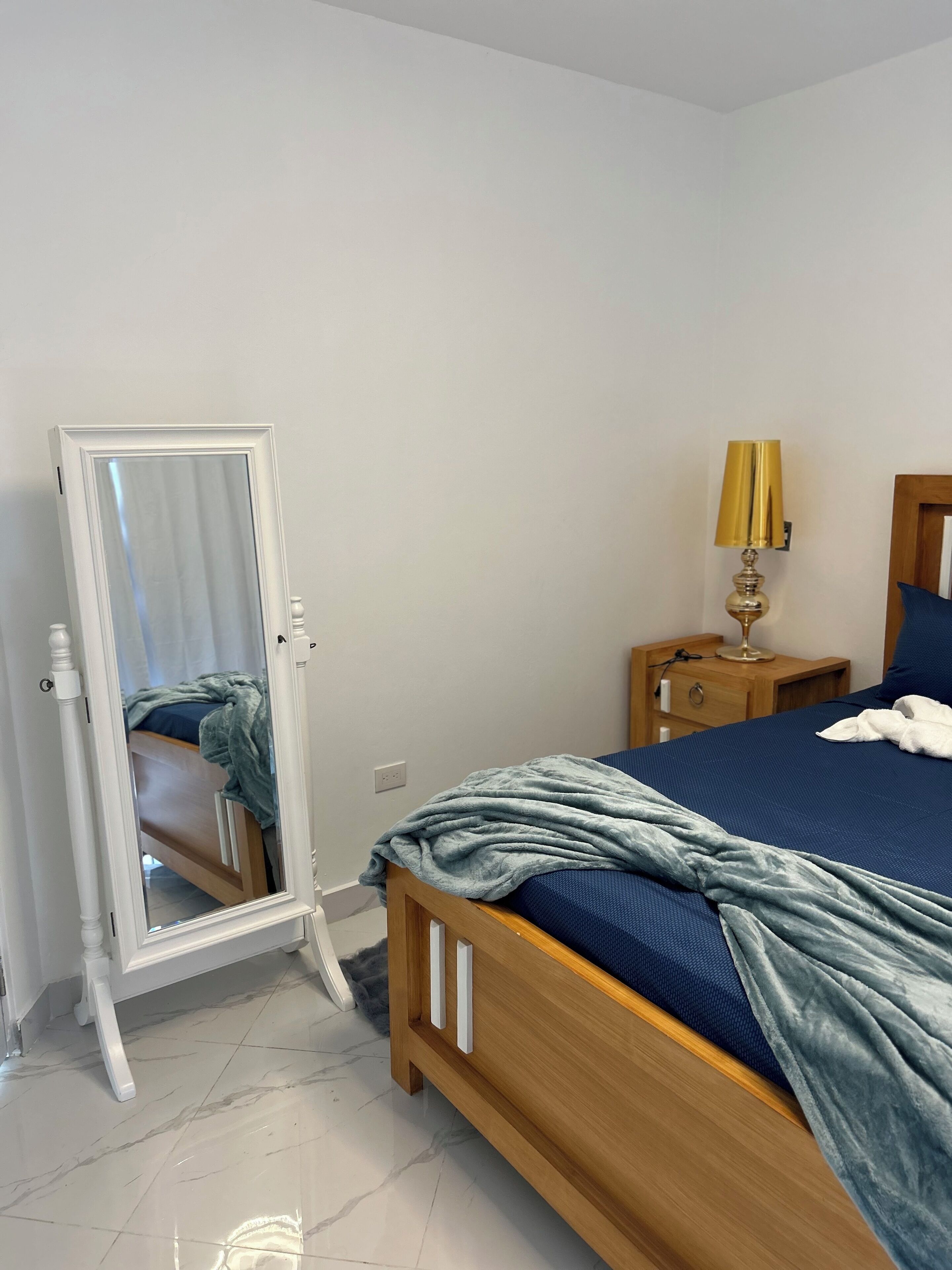 Ein Schlafzimmer mit einem hölzernen Bett, einem Nachttisch mit Lampe, einem Spiegel und einer blauen Decke.