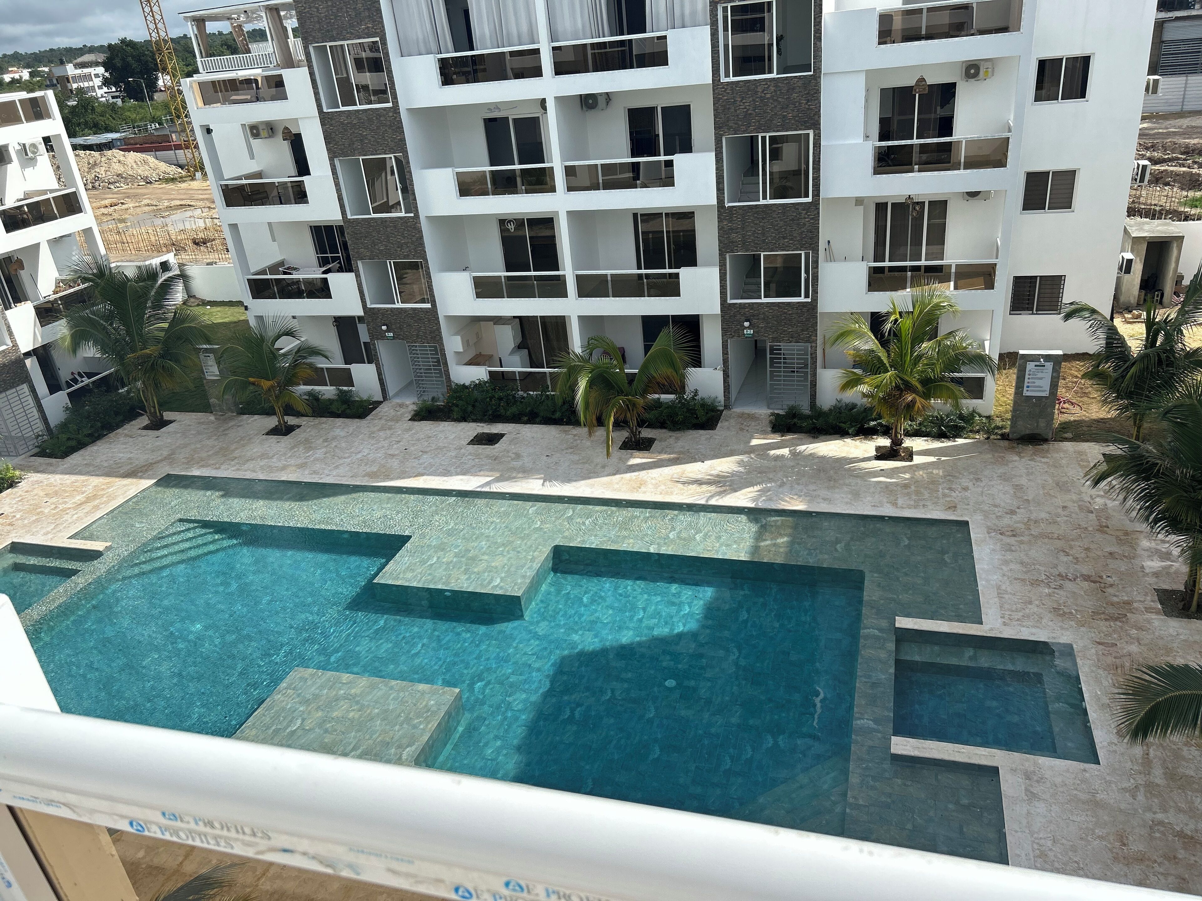 A modern apartment building with a swimming pool and palm trees.