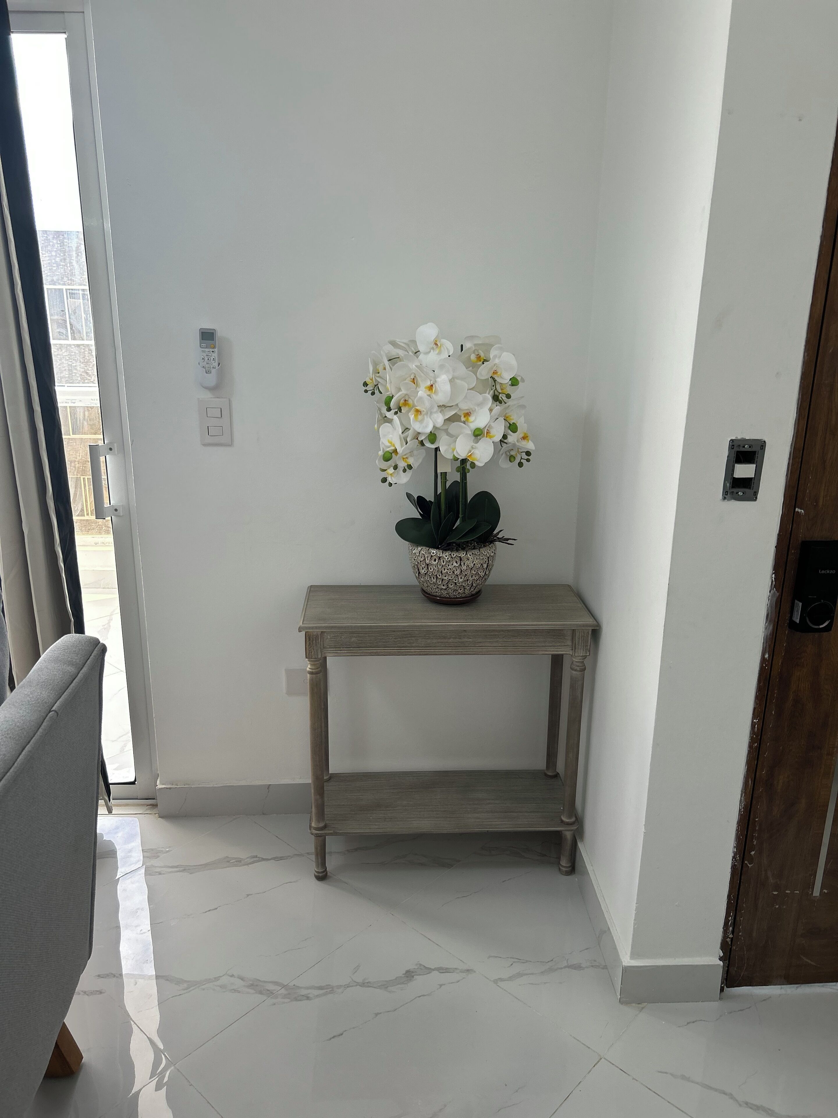 A hallway with a potted orchid on a wooden console table, a door, and a light switch on the wall.