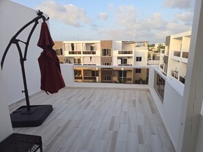 Un balcón con vistas a edificios cercanos, una lámpara de pie y un paraguas rojo.