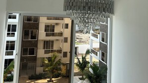 Ein Zimmer mit einem modernen Kronleuchter, einem großen Fenster mit Blick auf ein Gebäude und Palmen.