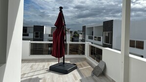 Ein Balkon mit einem roten Sonnenschirm, einer Steinsitzbank und Blick auf moderne Gebäude.