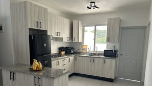 Eine moderne Küche mit hellen Holzschränken, einer Granit-Arbeitsplatte, einem schwarzen Kühlschrank, einem Herd und einer Mikrowelle.