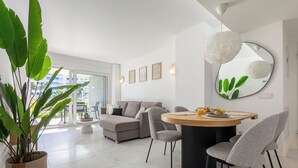 Ein modernes Wohnzimmer mit Essbereich, ausgestattet mit einem runden Tisch, grauen Stühlen, einem grauen Sofa und einer großen Topfpflanze.