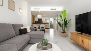 Ein modernes Wohnzimmer mit einem grauen Sofa, einem Couchtisch mit Sukkulente als Dekoration, einem Fernseher auf einem Holzboden und einem Essbereich im Hintergrund.