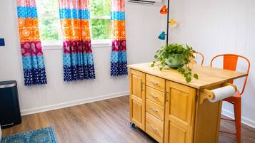 A room with a wooden cabinet, a chair, a plant, colorful curtains, and a window with an air conditioner.