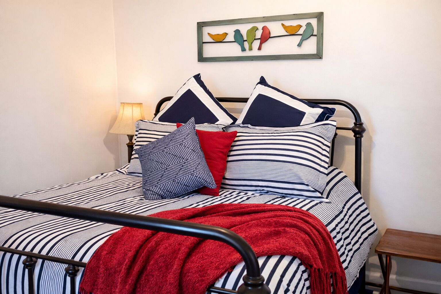 A bed with striped bedding, a red throw blanket, and multiple pillows.