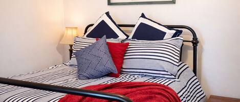 Una cama con ropa de cama a rayas, una manta roja y varias almohadas.