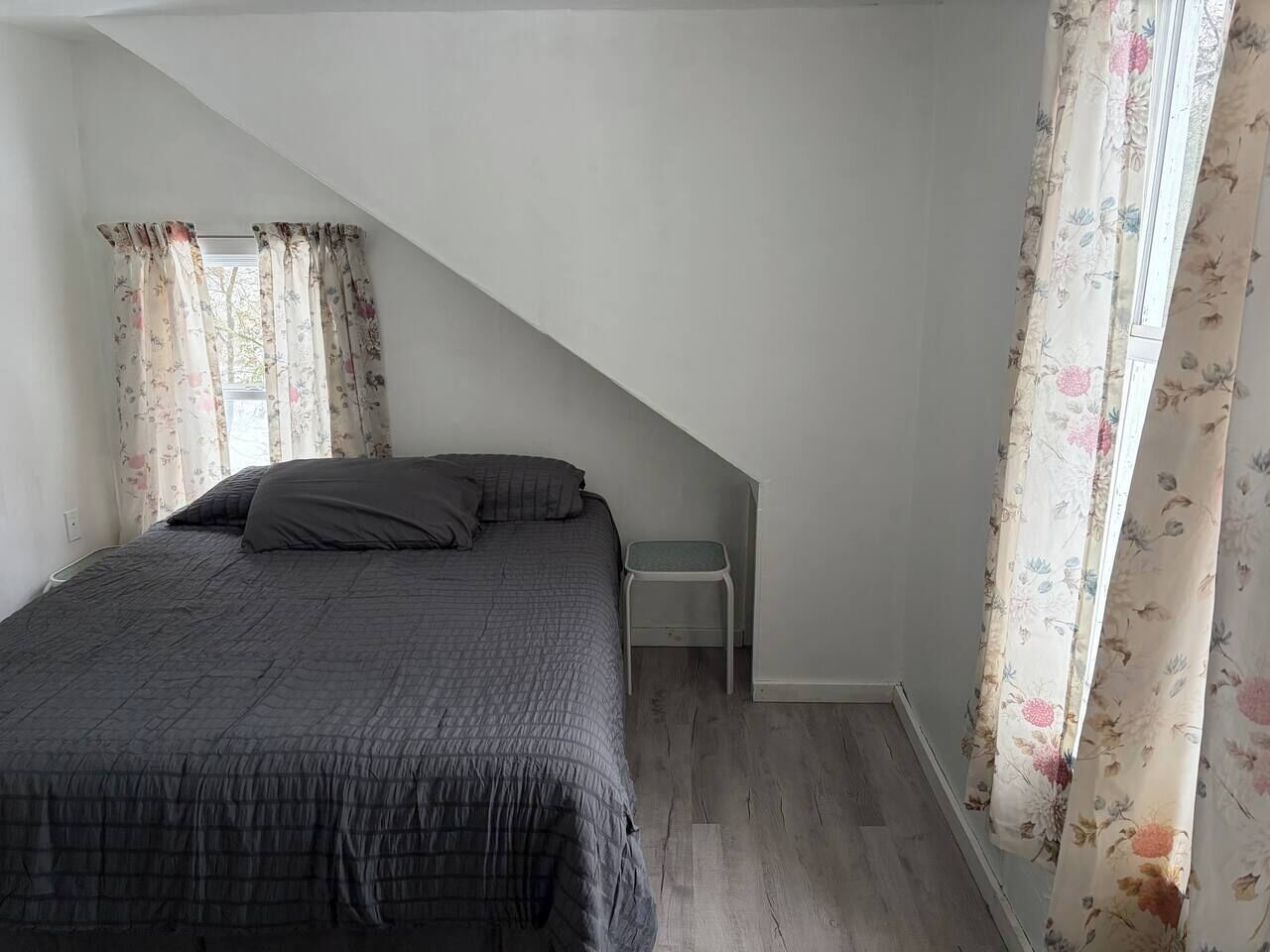 Une chambre à coucher avec un lit, une table de chevet et une fenêtre ornée de rideaux à motifs floraux.