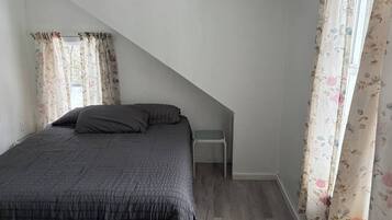 Une chambre à coucher avec un lit, une table de chevet et une fenêtre ornée de rideaux à motifs floraux.
