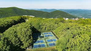 An aerial view of a tennis court surrounded by dense forest and hills.