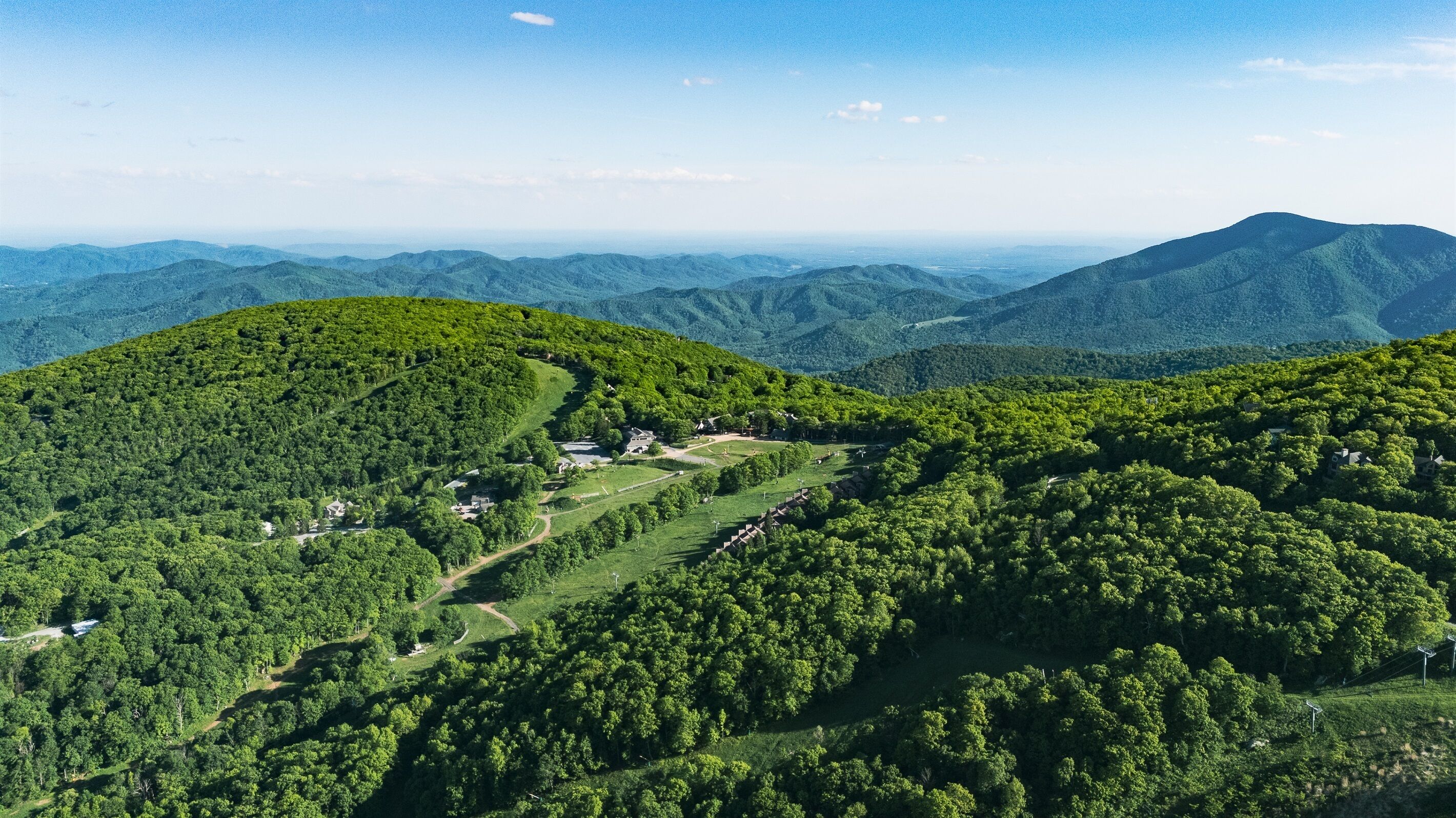 A mountainous landscape with a small cluster of buildings surrounded by dense forest.